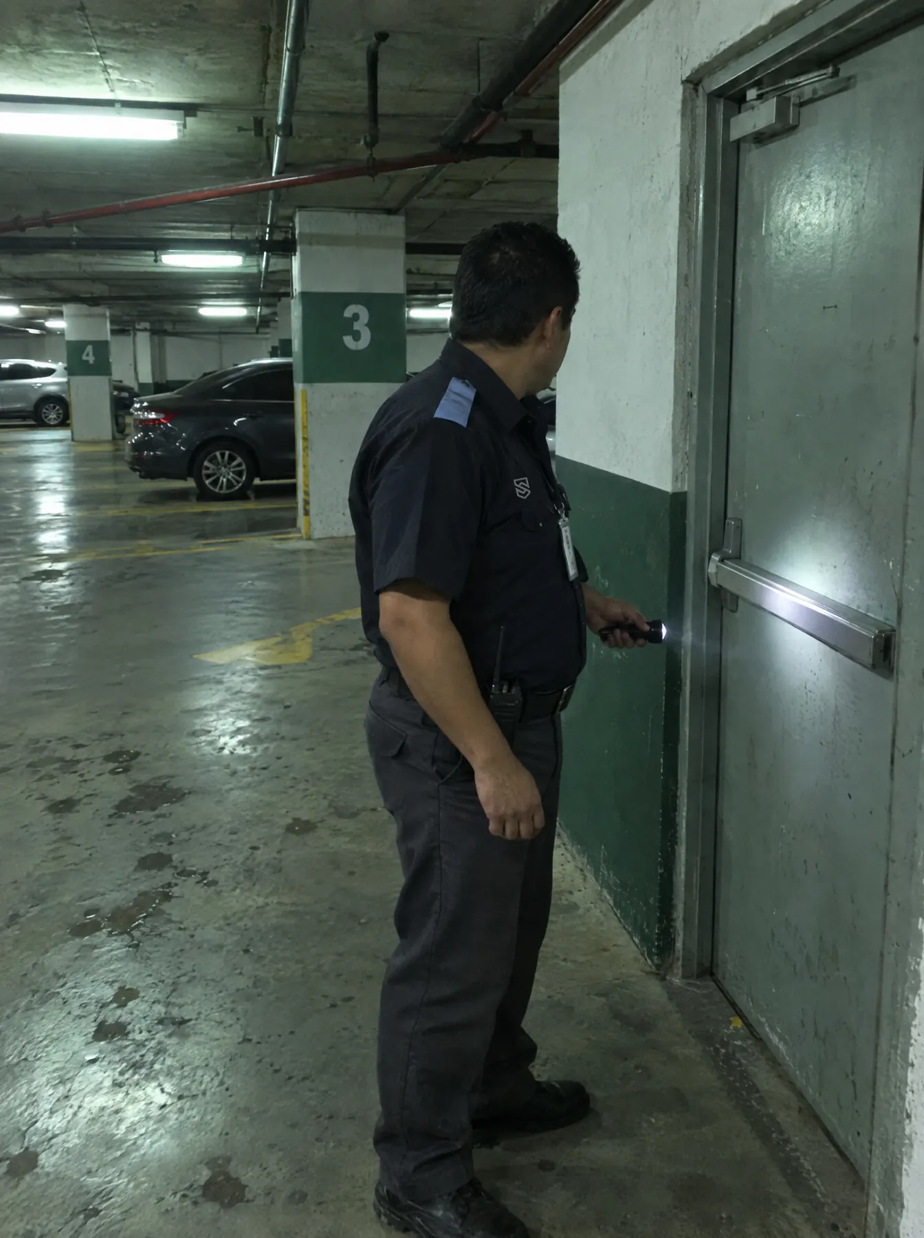 Guardia revisa que una salida de emergencia esté cerrada durante un rondín nocturno en un estacionamiento subterráneo